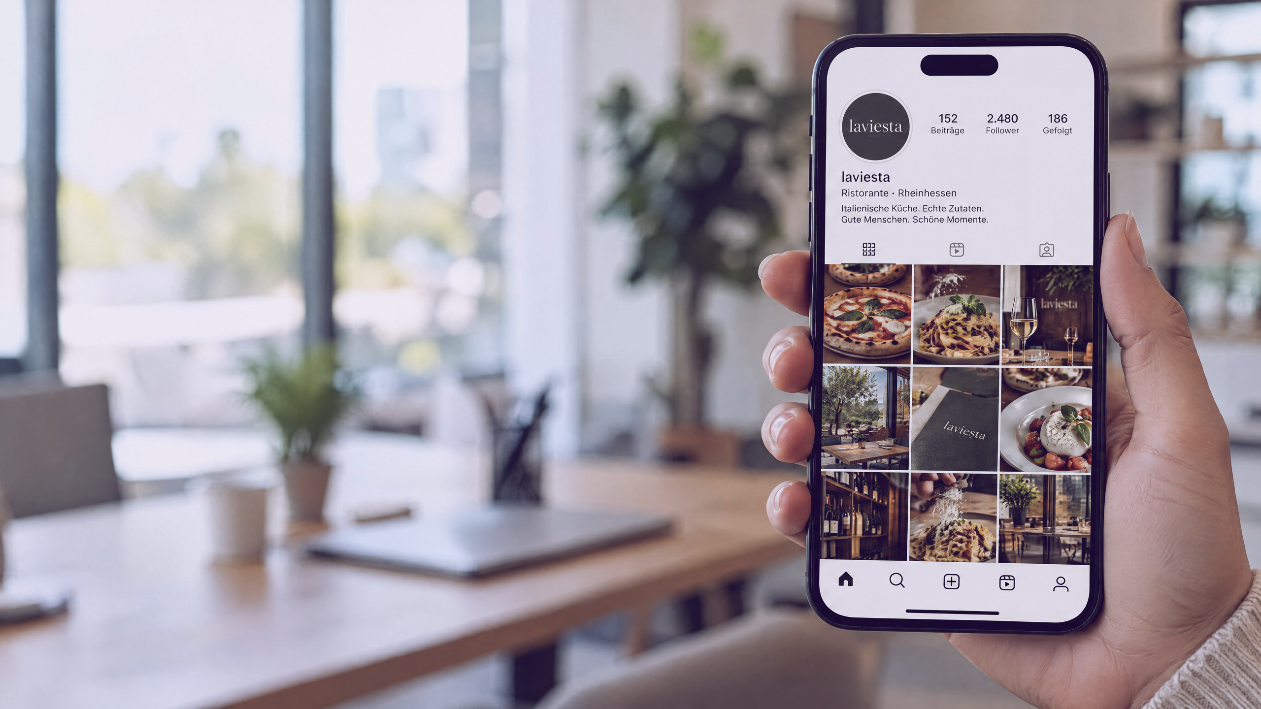 Hand mit Handy, darauf das Profil eines Restaurants